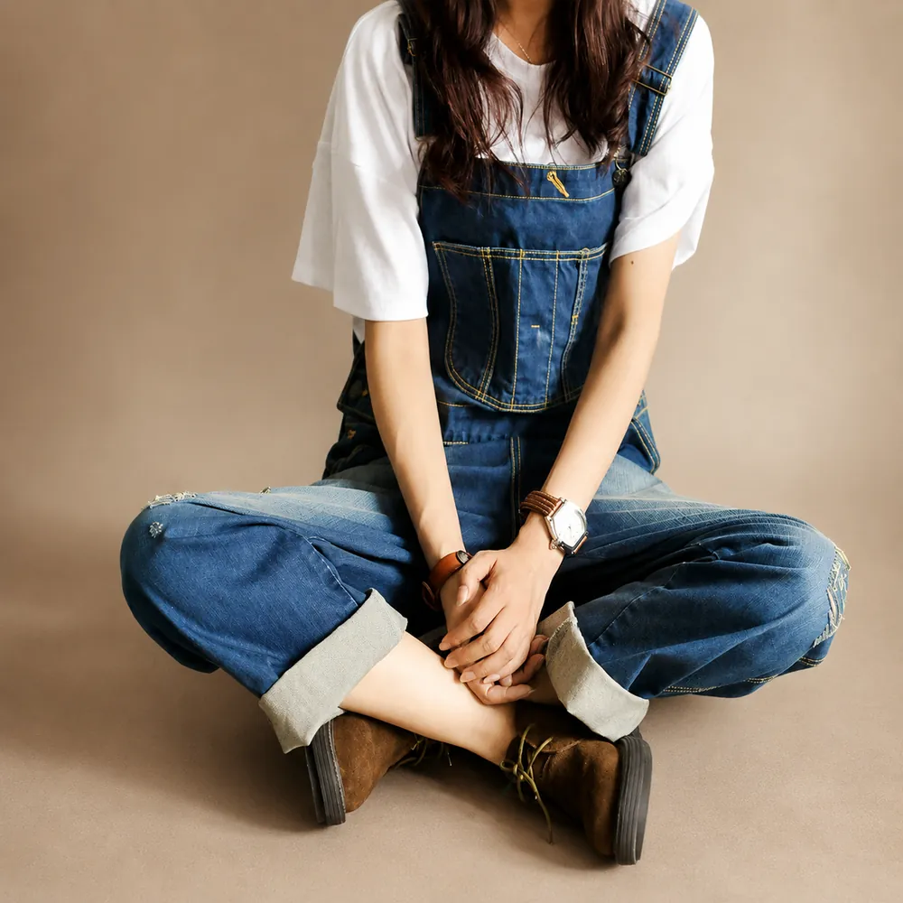 Model seated on the studio floor in indigo denim dungarees